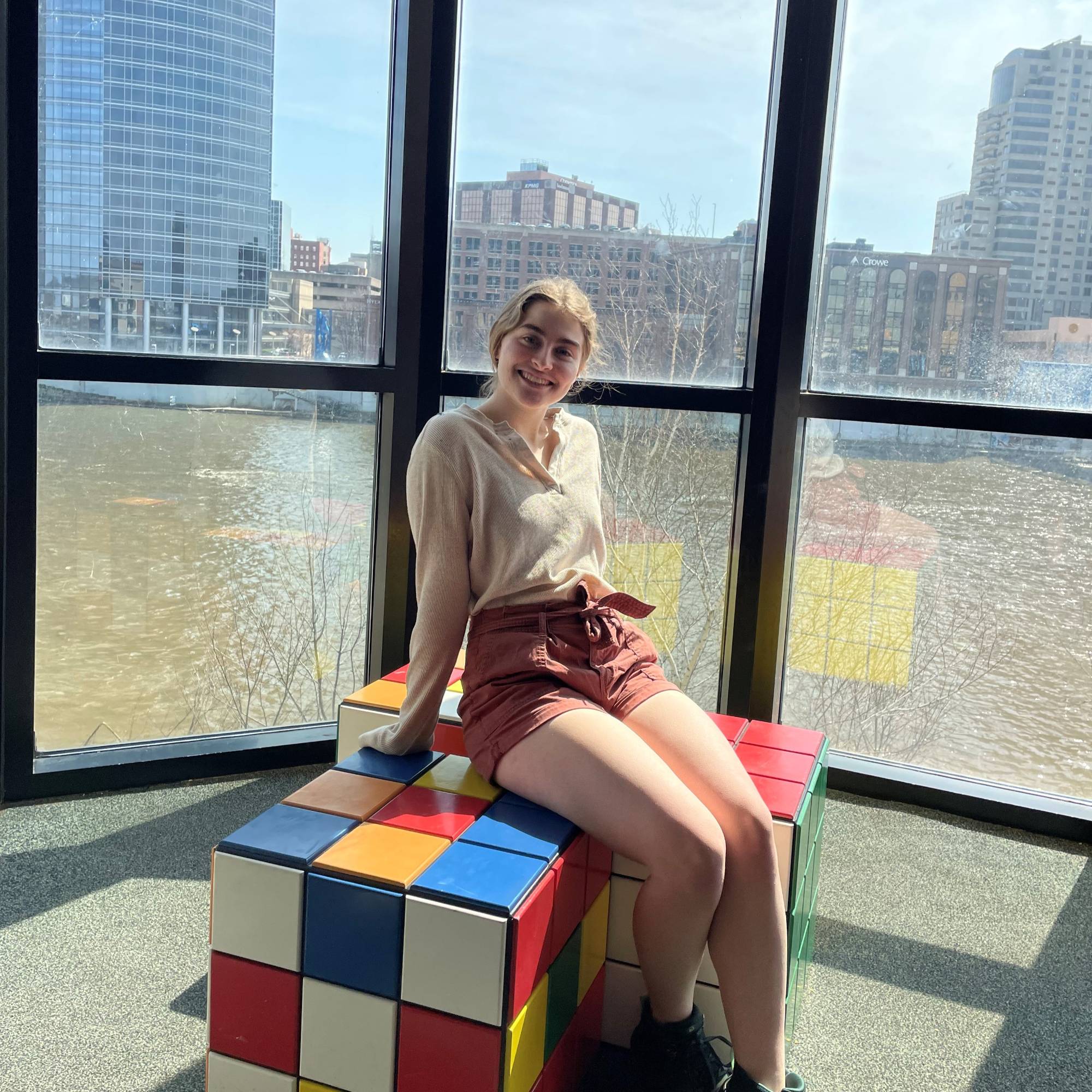 Smiling girl siting on giant rubix cube in front of window